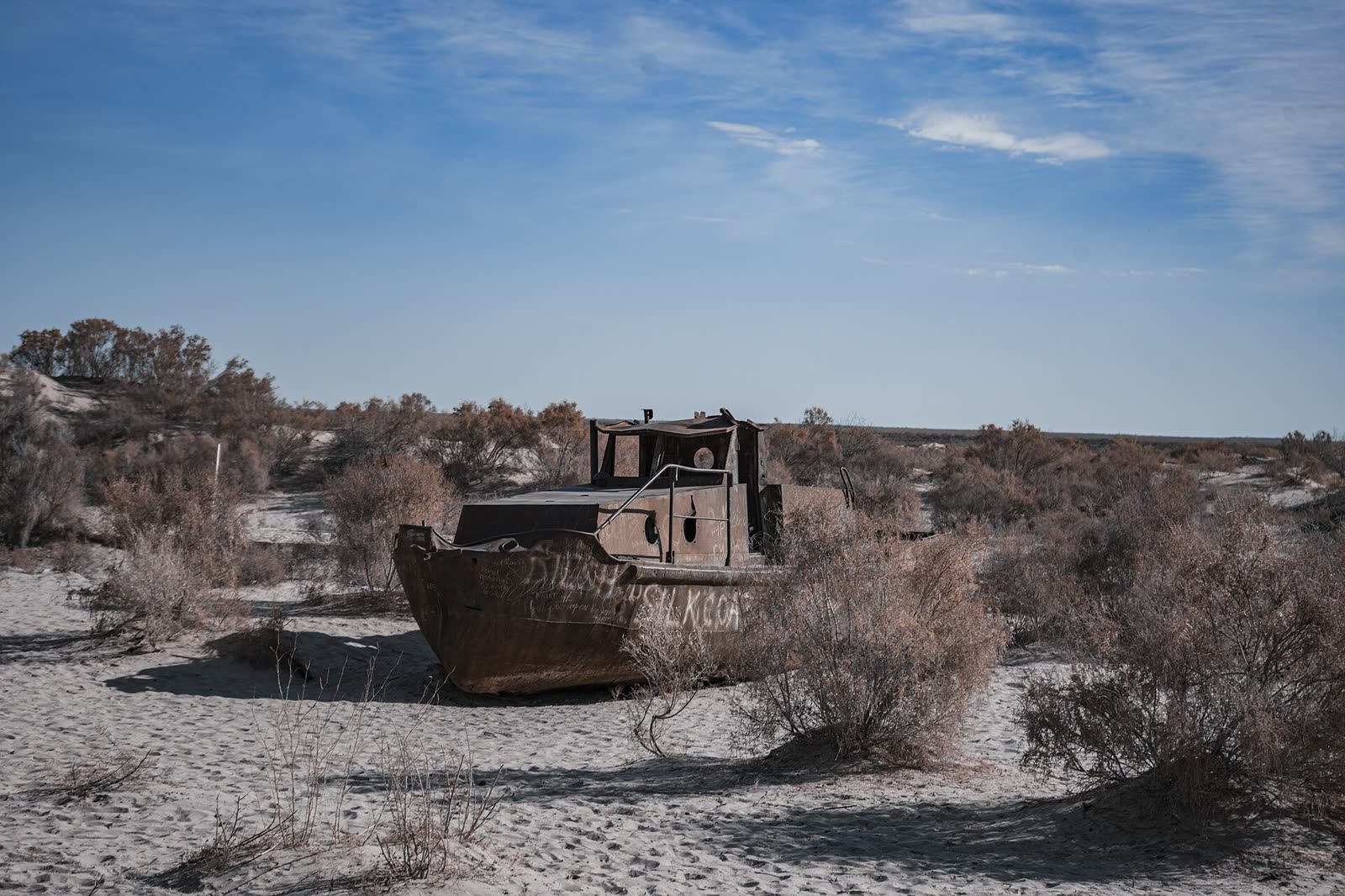 A rusted fishing boat stranded on the dry former bed of the Aral Sea at Moynaq, Uzbekistan, under a wide blue sky
